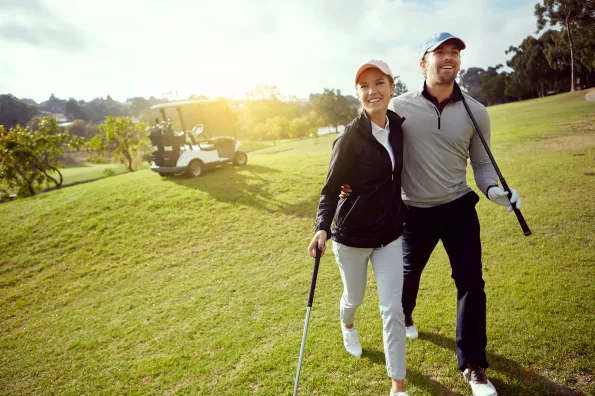 A couple walking the golf course with cart in the background